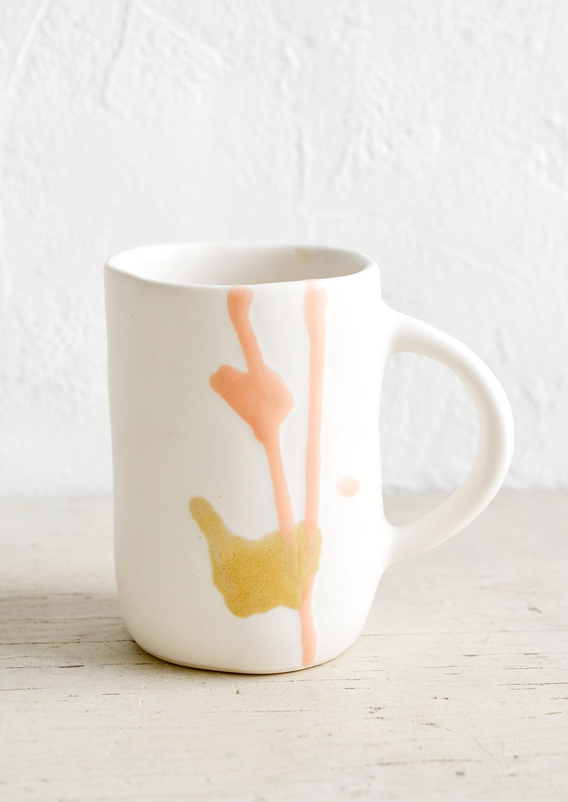 A tall white ceramic mug with peach and mustard glaze drip detail.