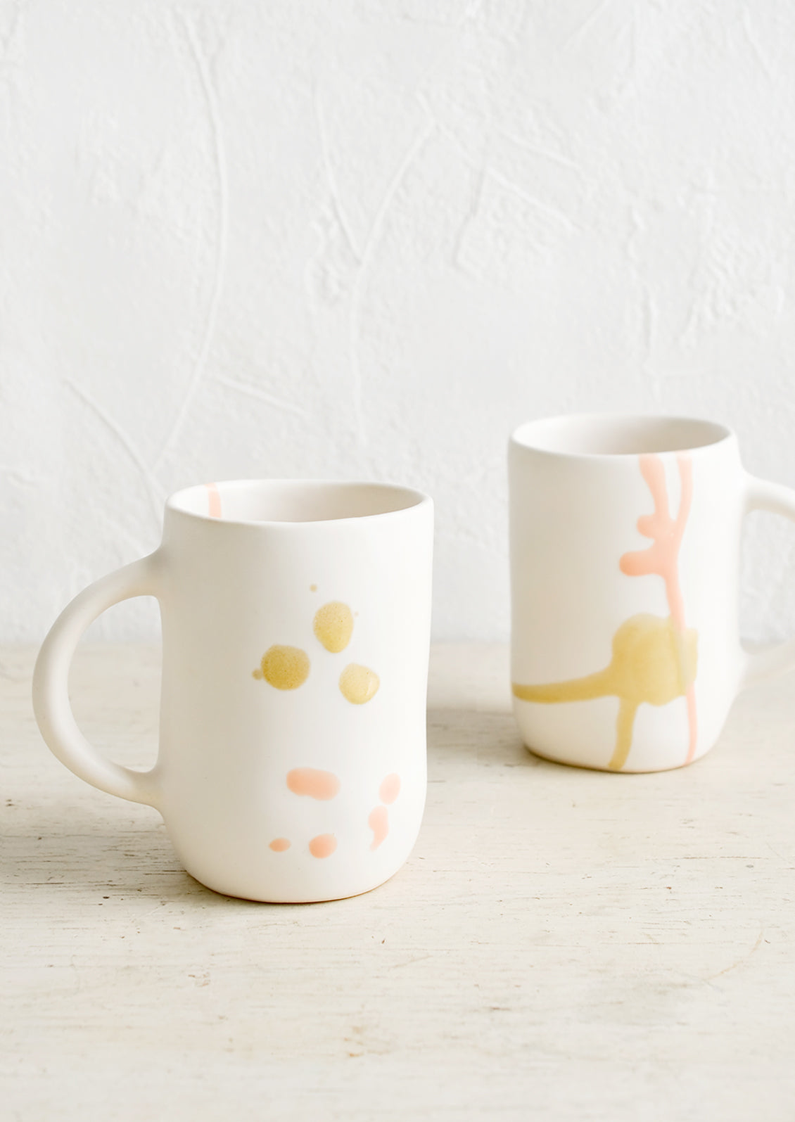 Two white ceramic mugs with hand painted peach and mustard glaze drips.