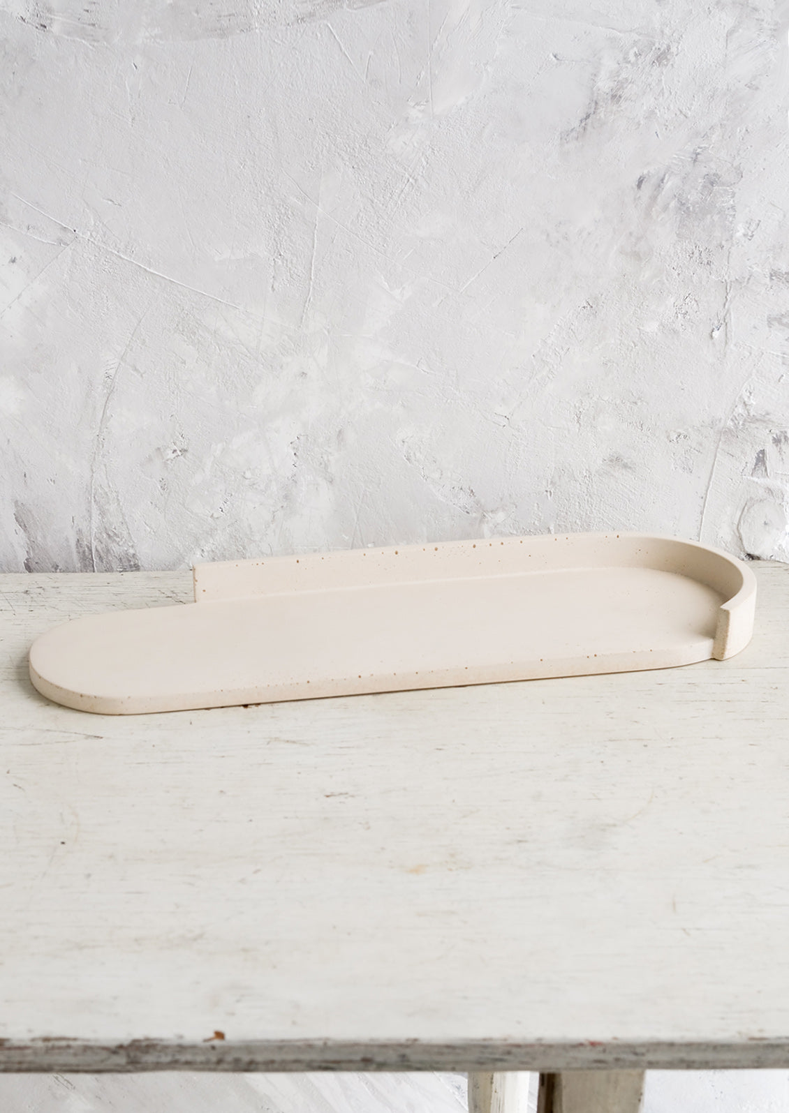 An elongated oval shaped platter made from straw colored concrete.