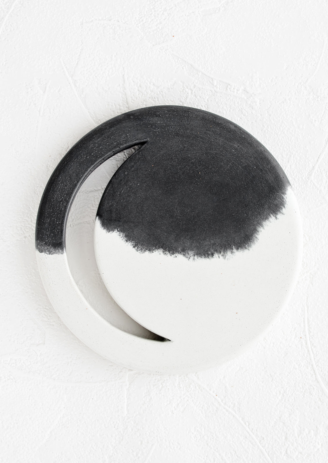A round concrete trivet in black and white with crescent moon shaped cutout.