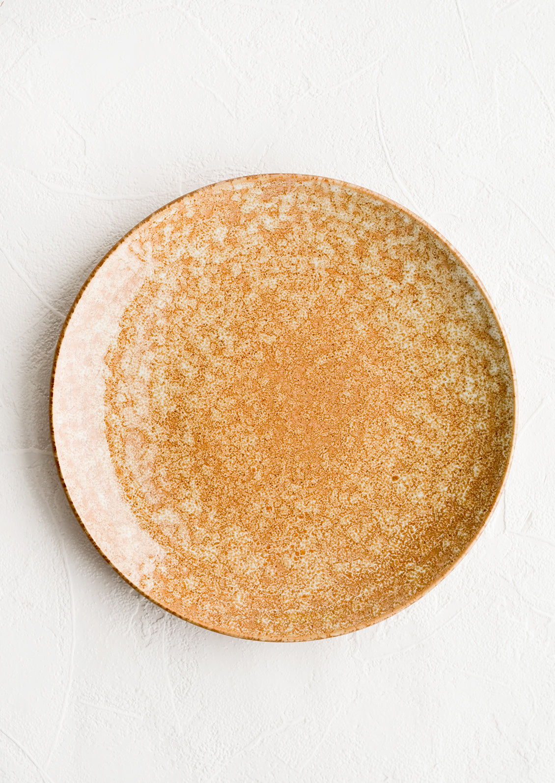 A round ceramic plate in dappled, glossy light brown glaze.