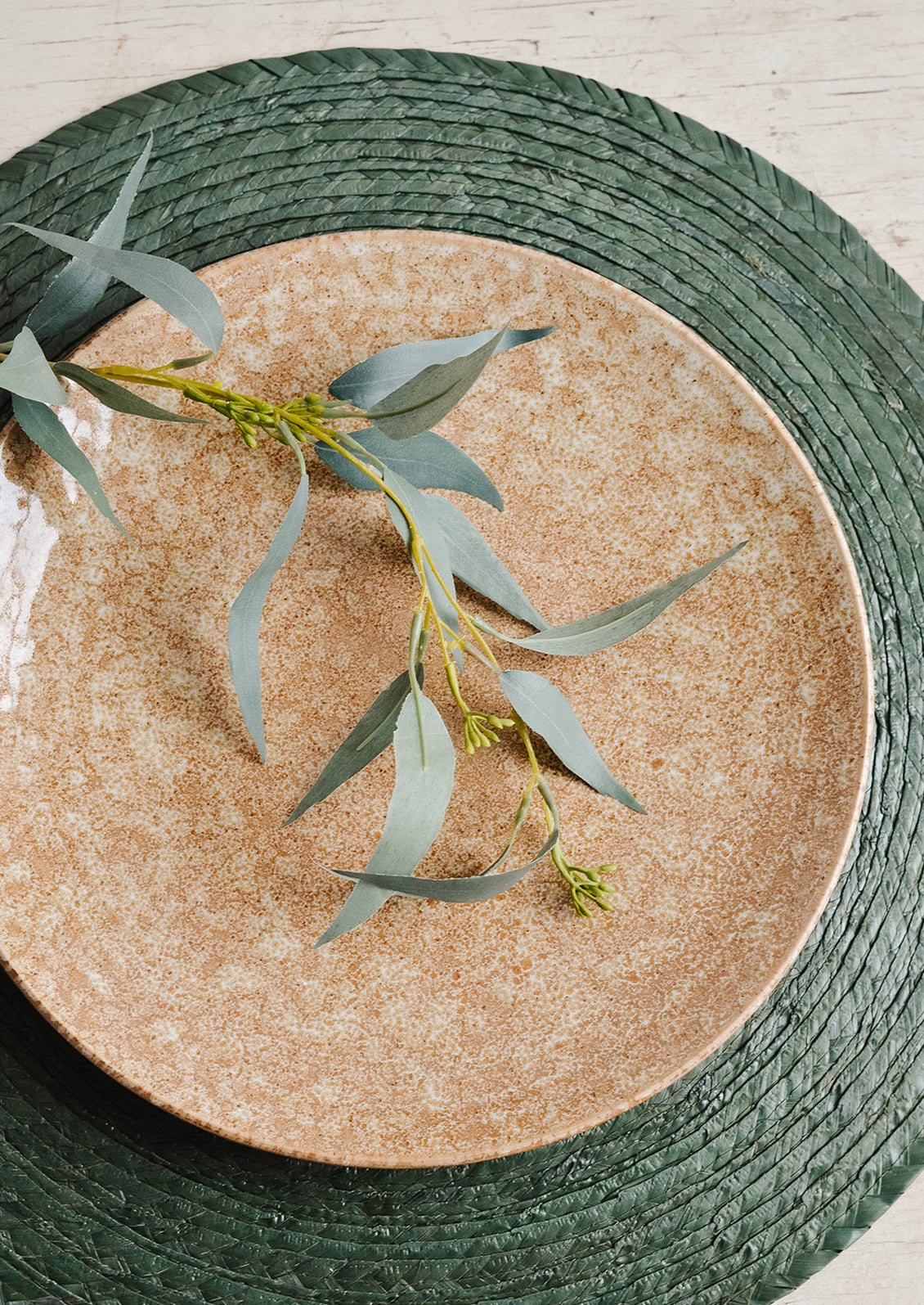 A brown ceramic plate on a dark green woven placemat with eucalyptus garnish.