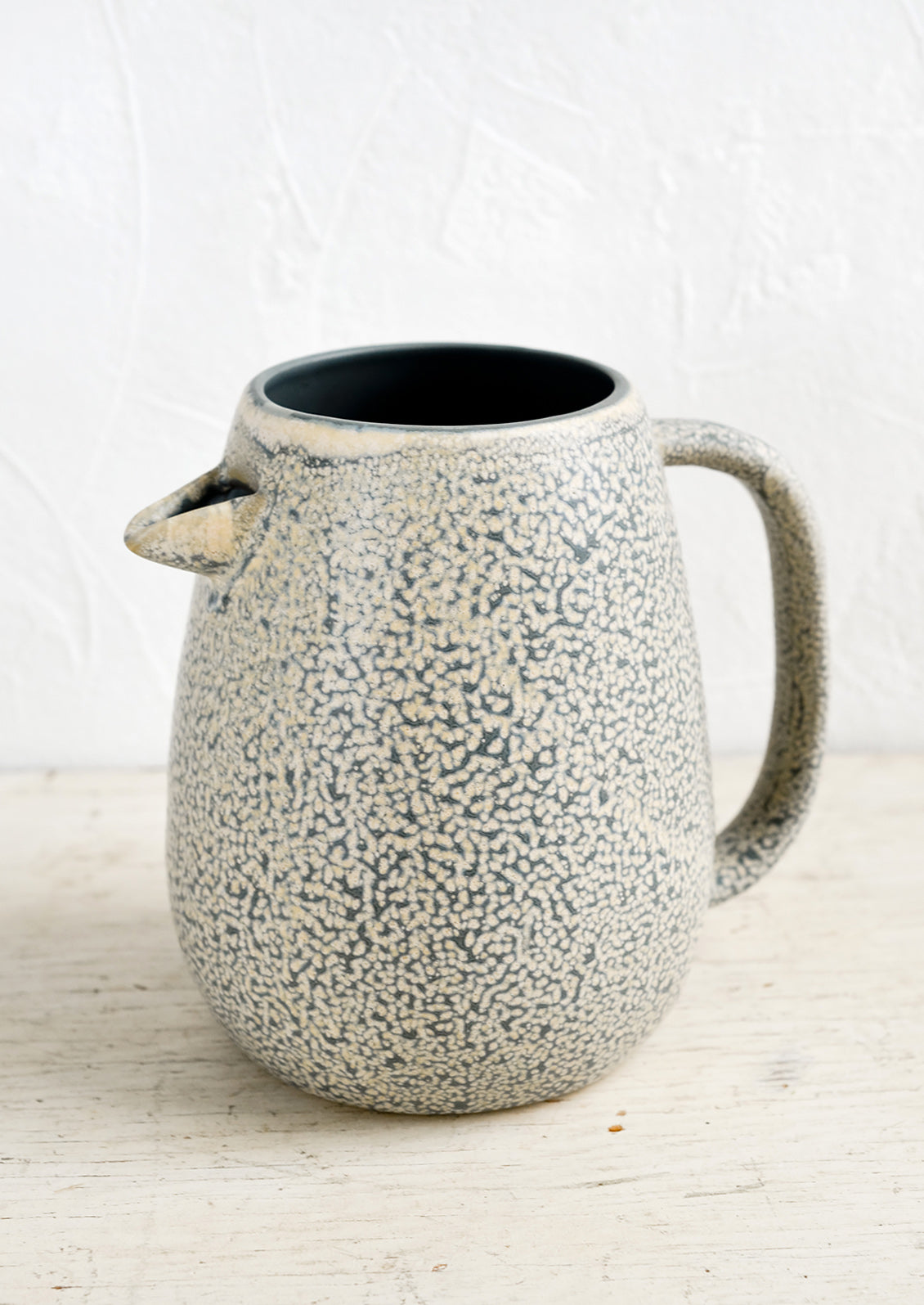 A ceramic pitcher with built-in spout in speckled grey and natural glaze.