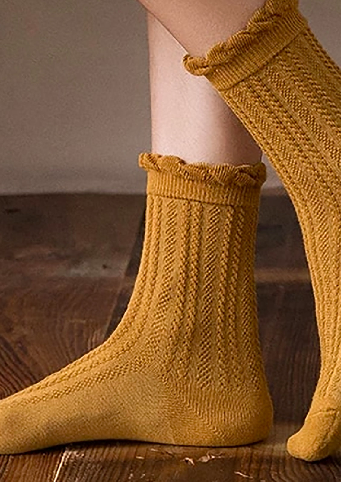 A pair of feet wearing cable knit socks that hit above the ankle.