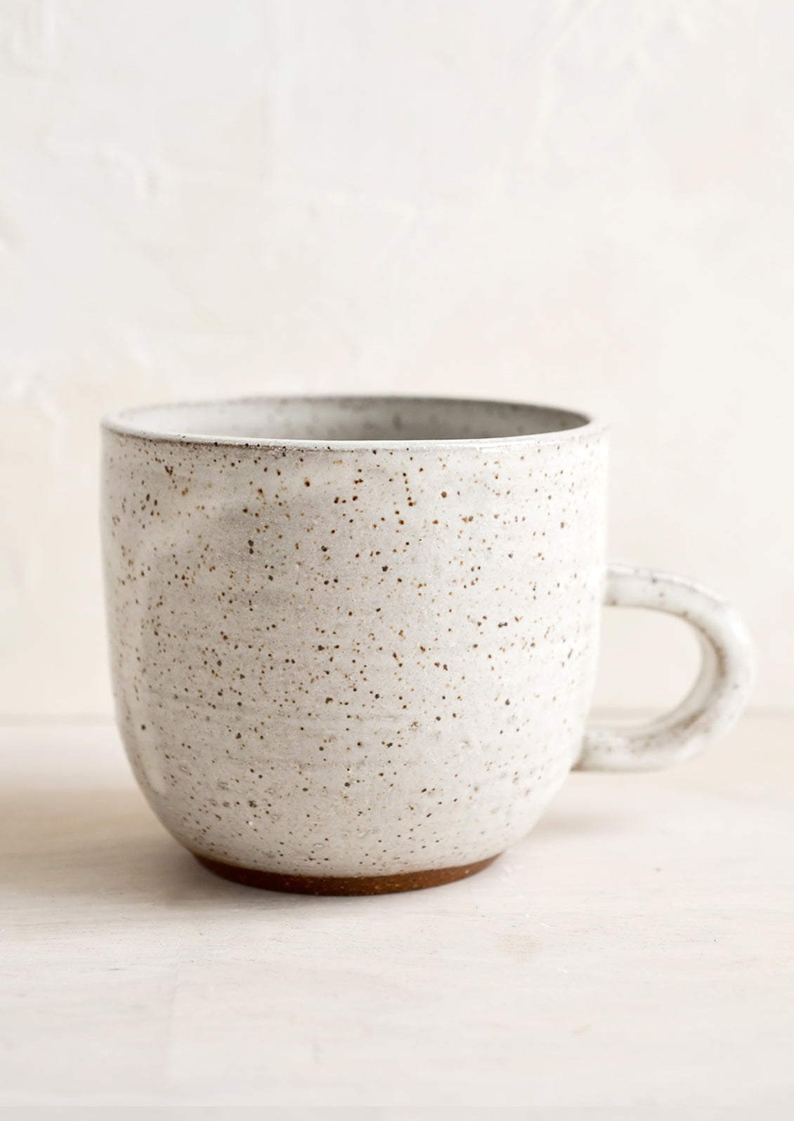 A short ceramic coffee mug in glossy natural glaze with brown speckles.