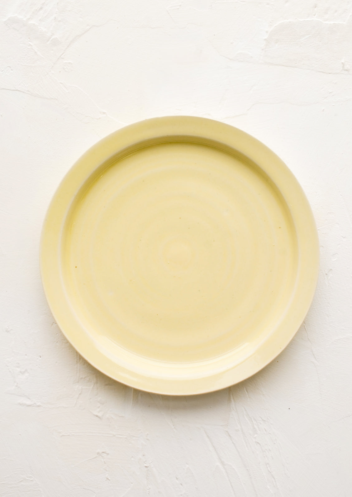 A ceramic side plate in glossy butter yellow glaze.