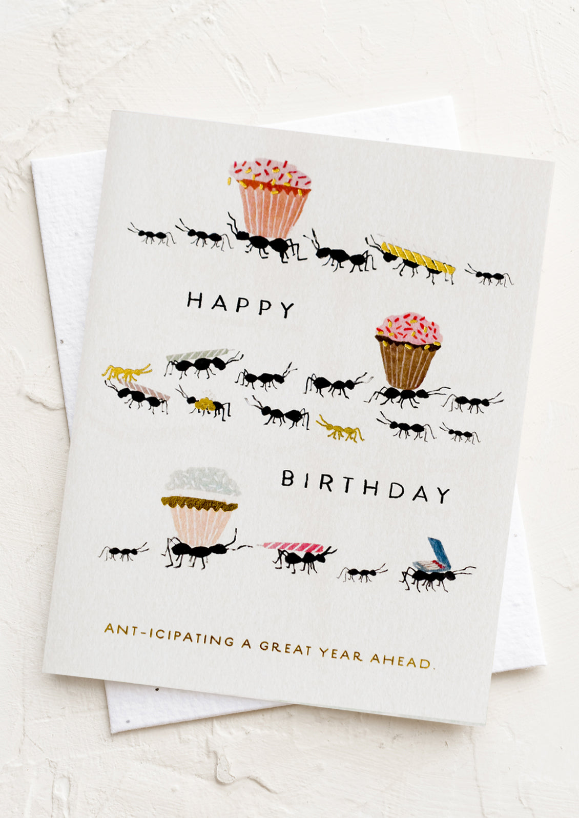 A card with illustration of ants carrying around cupcakes and birthday candles, text reads "Ant-icipating a great year ahead".