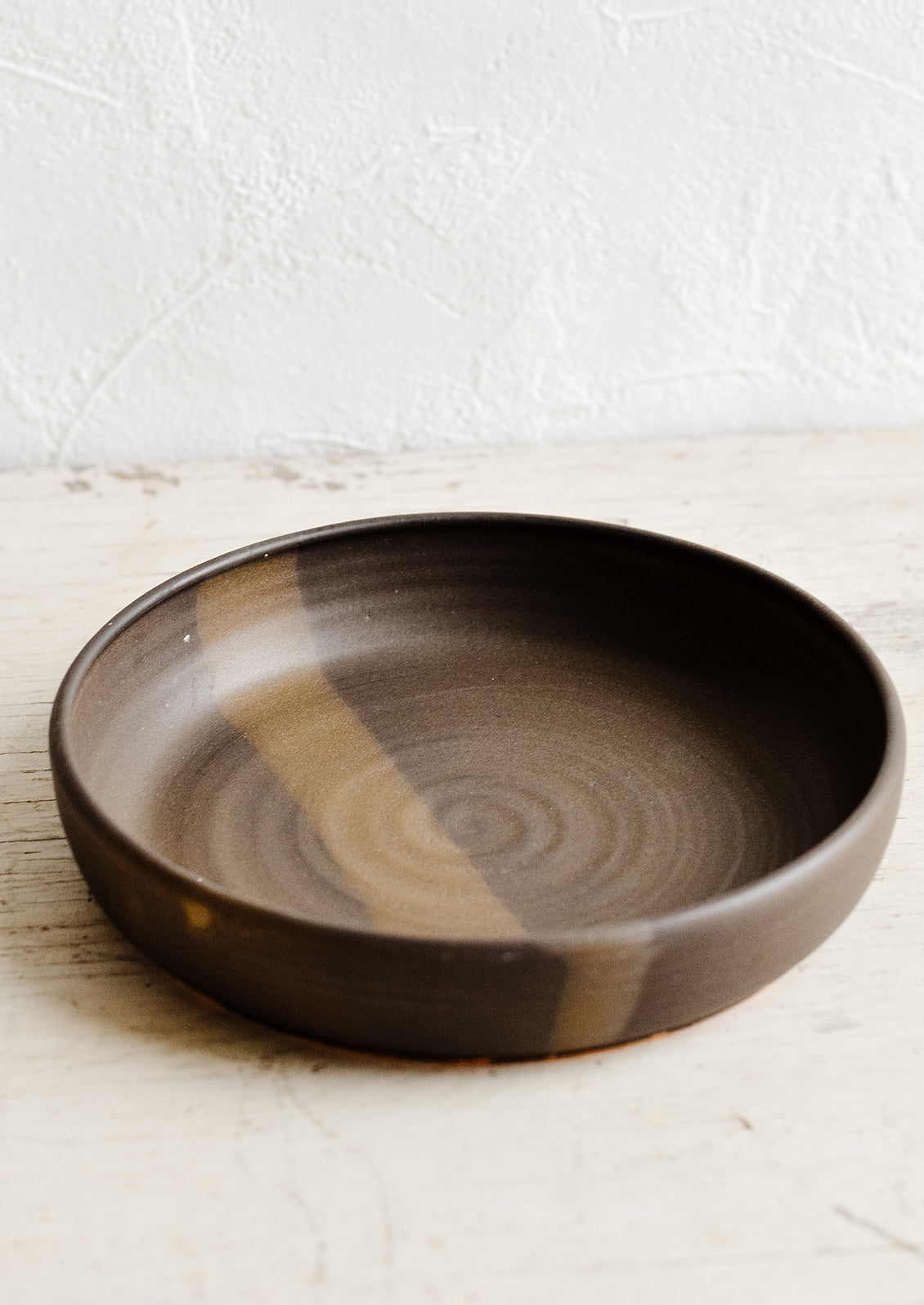 A wide and shallow ceramic bowl in matte brown.