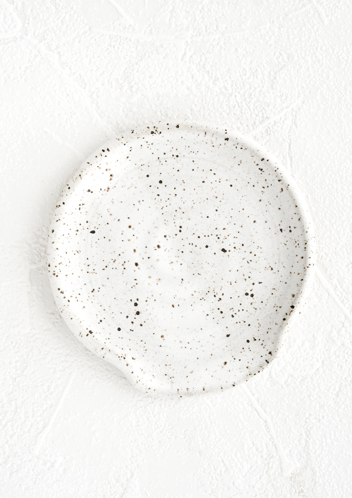 A round, handmade ceramic spoon rest in a speckled matte white glaze.