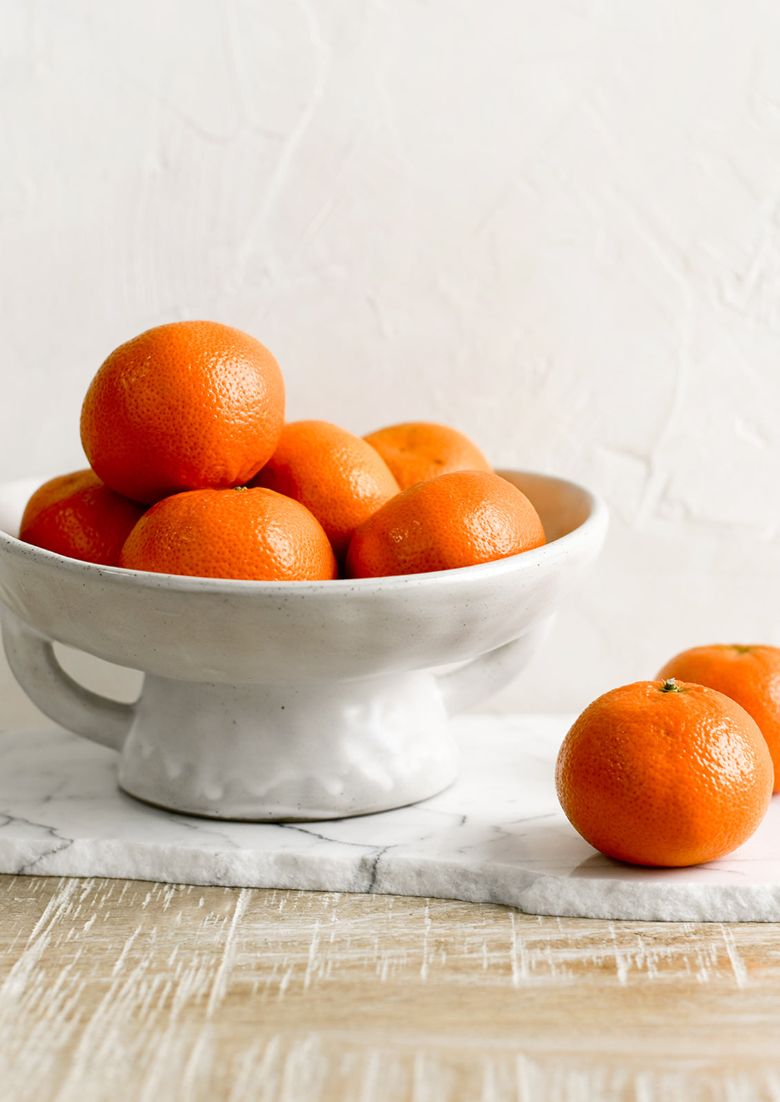 A footed ceramic bowl holding oranges.