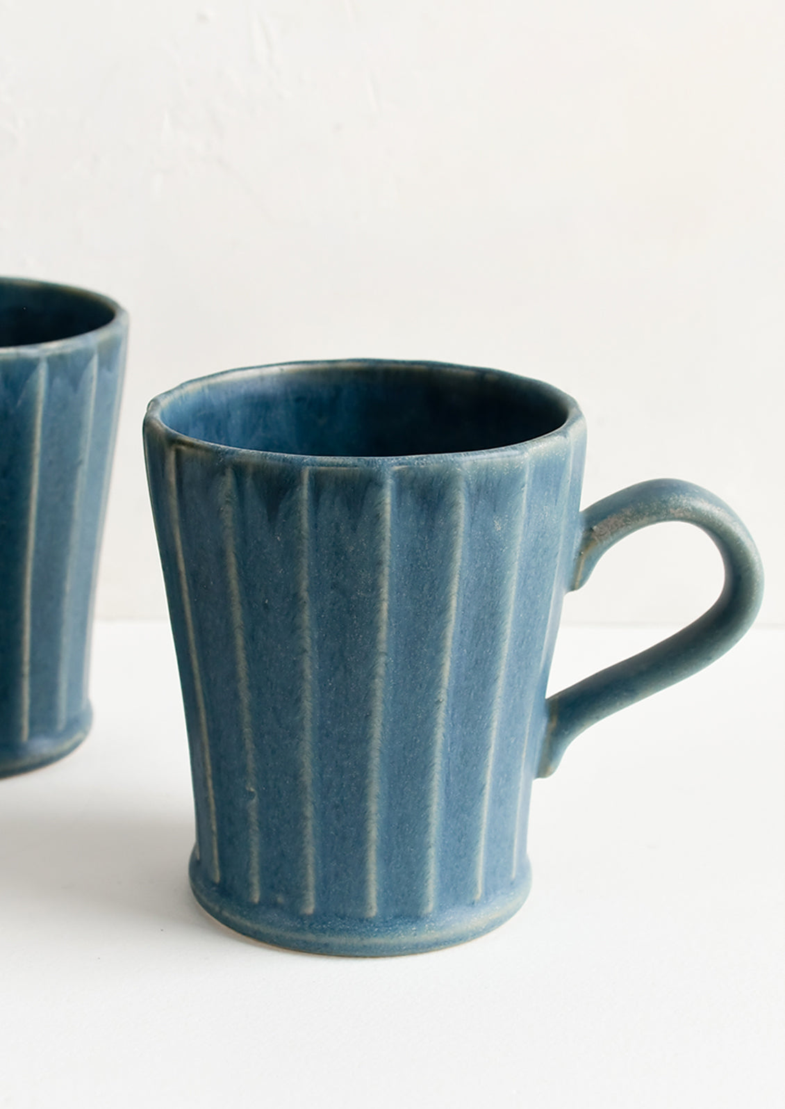Blue ceramic mugs with fluted texture and tapered bottom.