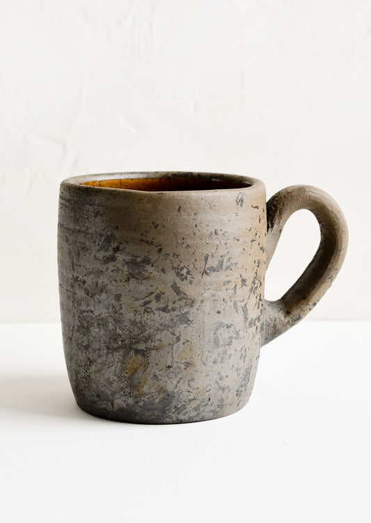 A coffee mug made from raw, unglazed dark brown clay.