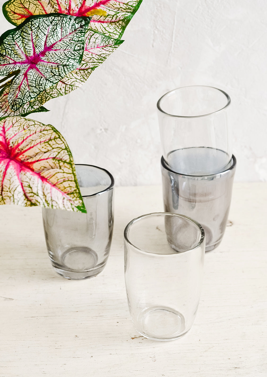 Clear and grey glass cups on a table with plant