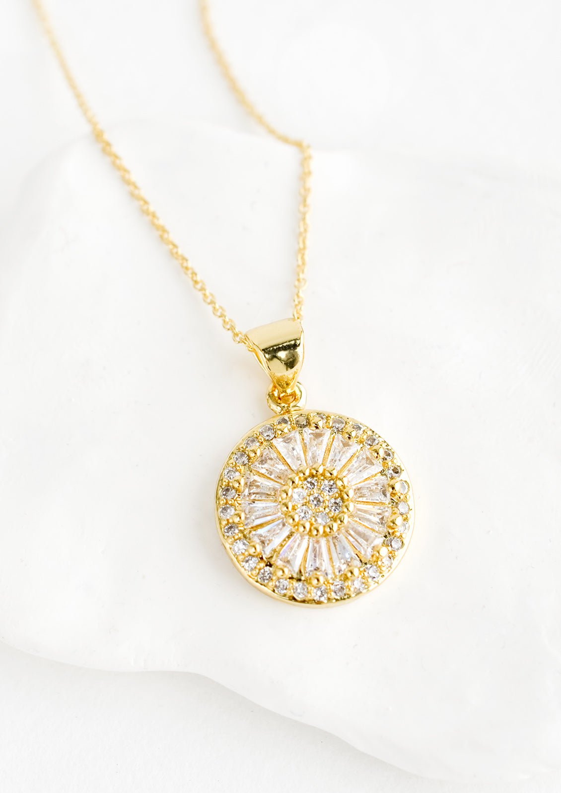 A gold necklace with round pendant encrusted with clear crystals.