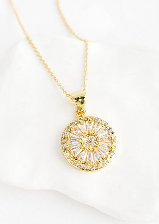 A gold necklace with round pendant encrusted with clear crystals.