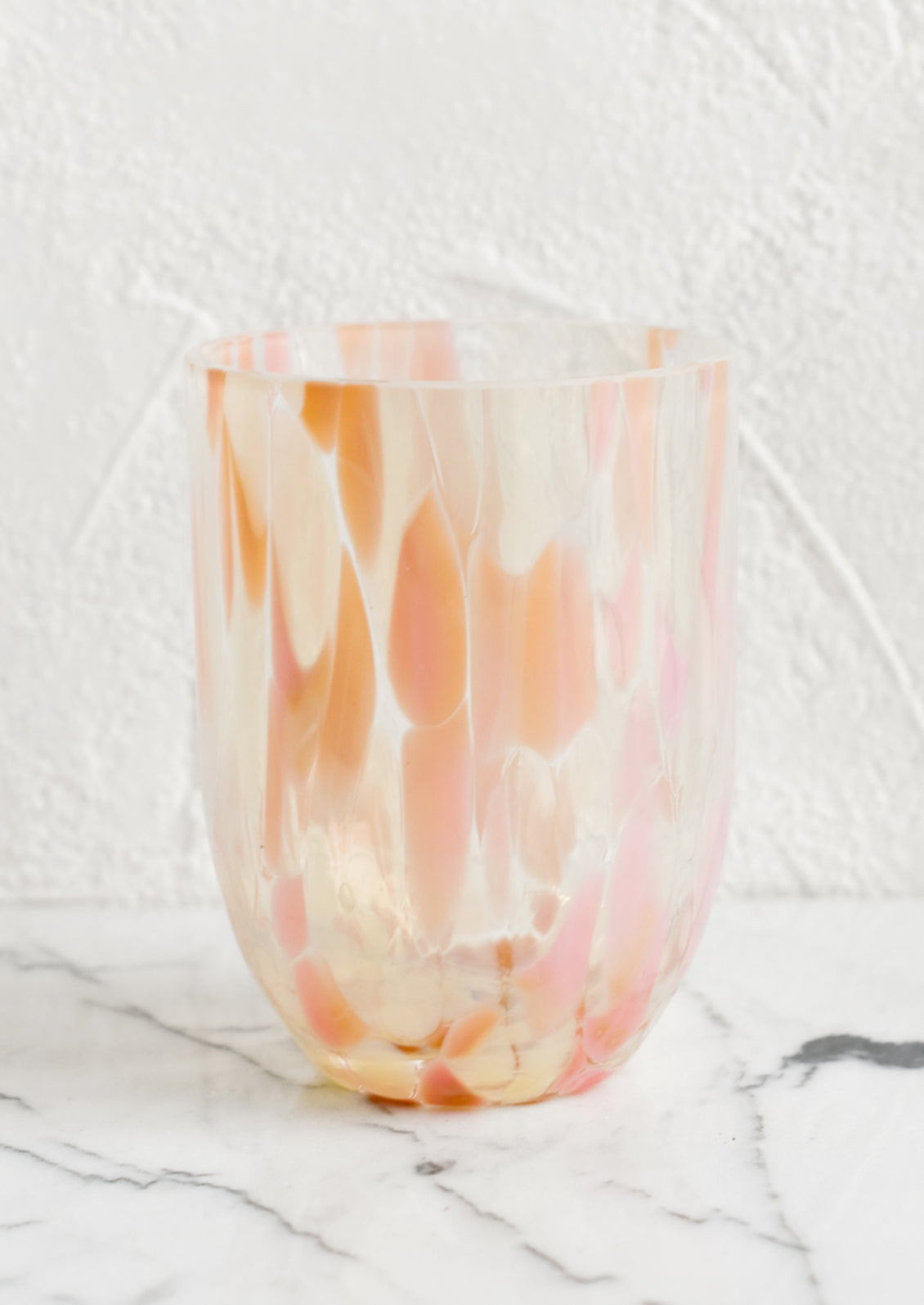 A handmade speckled glass juice cup with peach and pink spots.