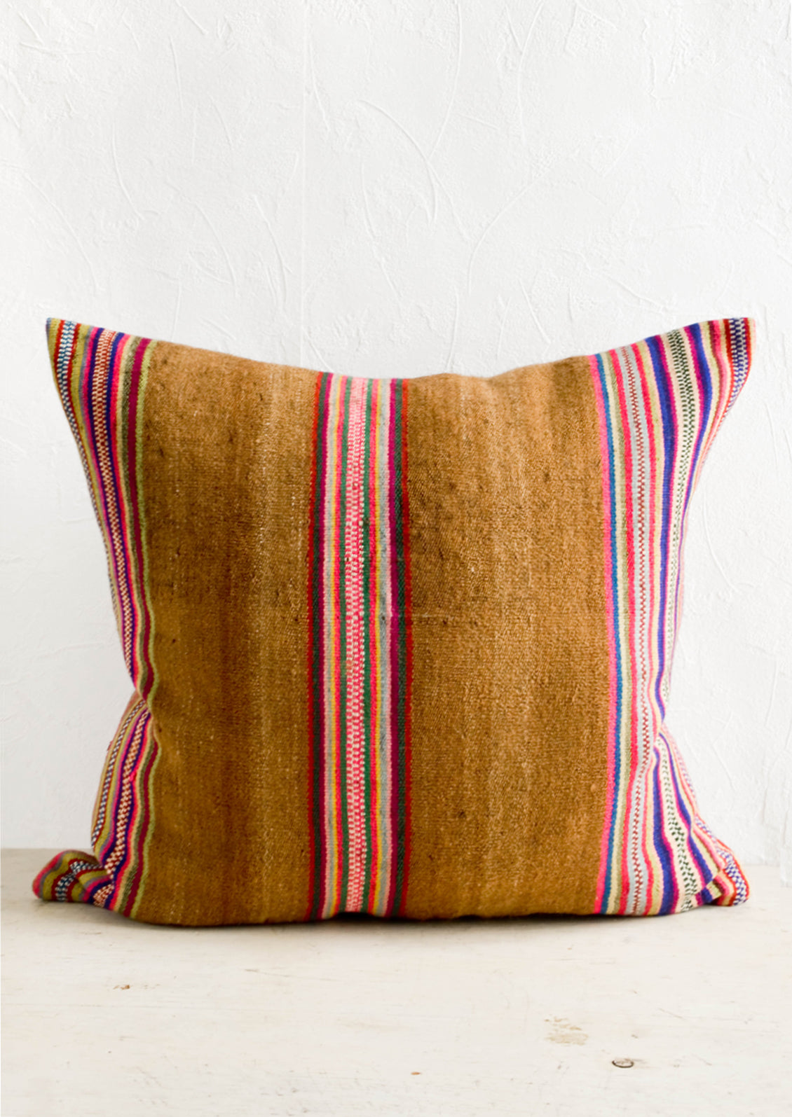 Square throw pillow in striped vintage wool fabric. Brown with colorful rainbow stripes.