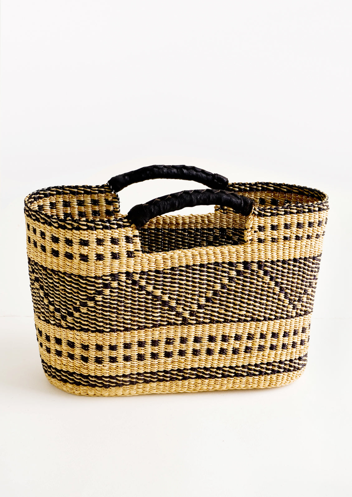 Woven tote made from natural and black dried grass, with geometric design and leather cutout handles