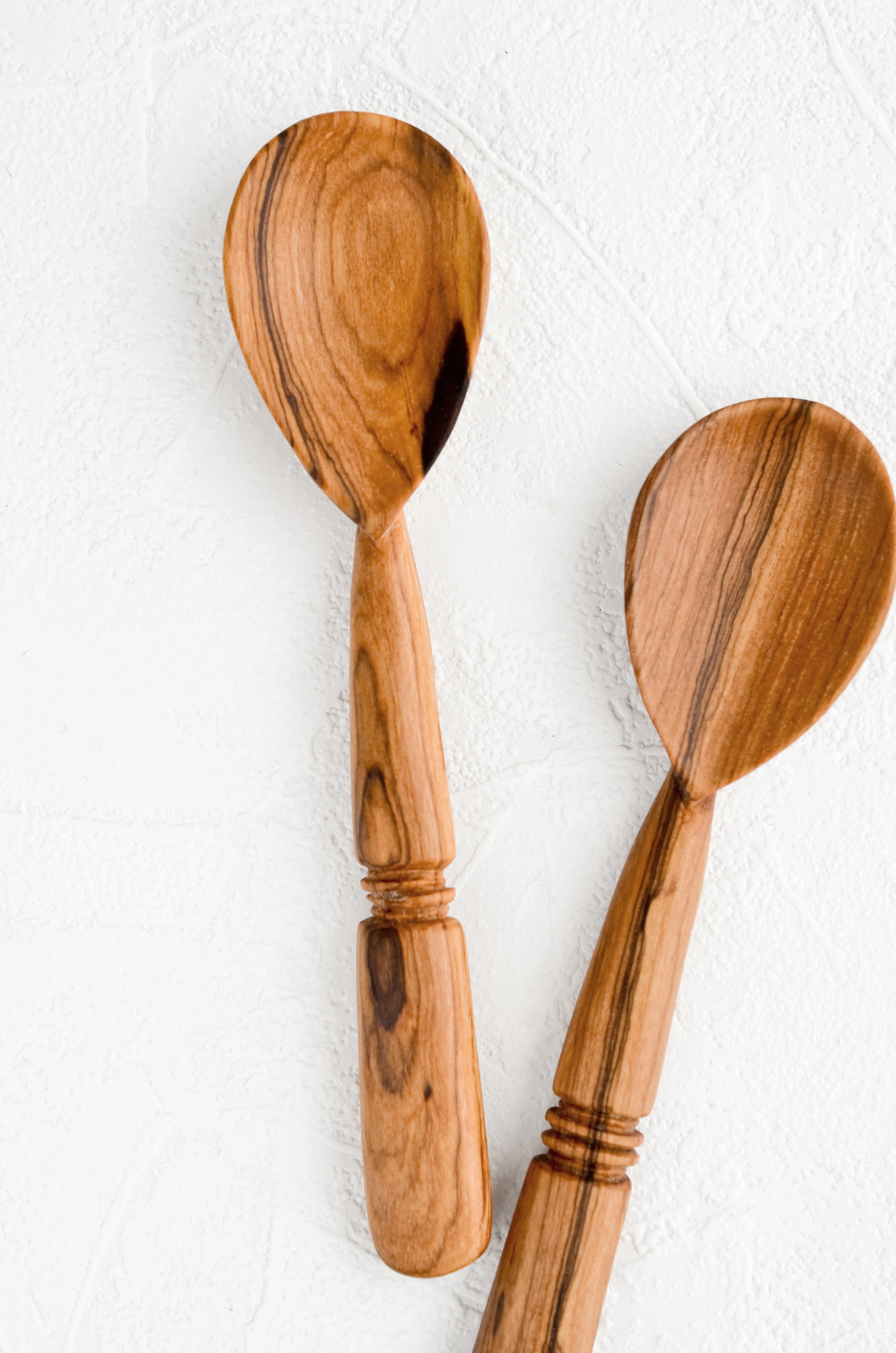 Two hand-carved spoons made from olivewood, each with its own unique grain pattern.