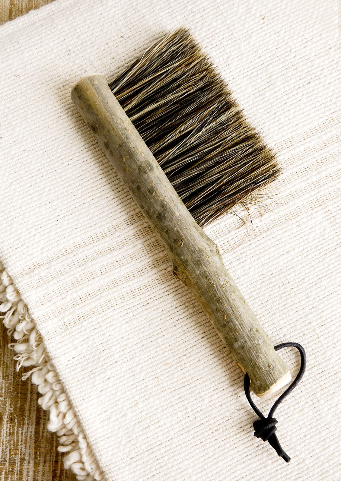 Bristle brush with natural bark handle and leather tie at end