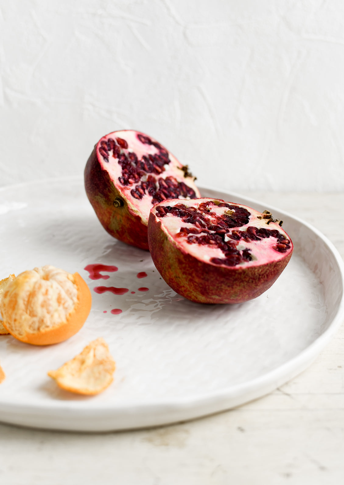 A round white ceramic tray with basketweave texture, styled with a pomegranate.