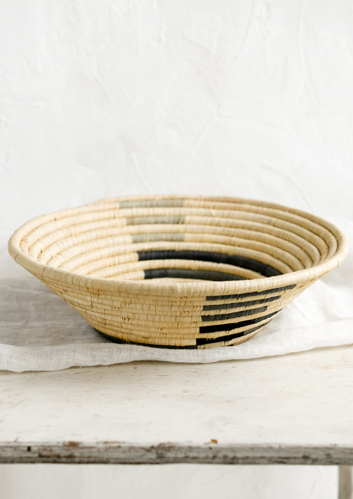 A round raffia bowl with grey spiral pattern.