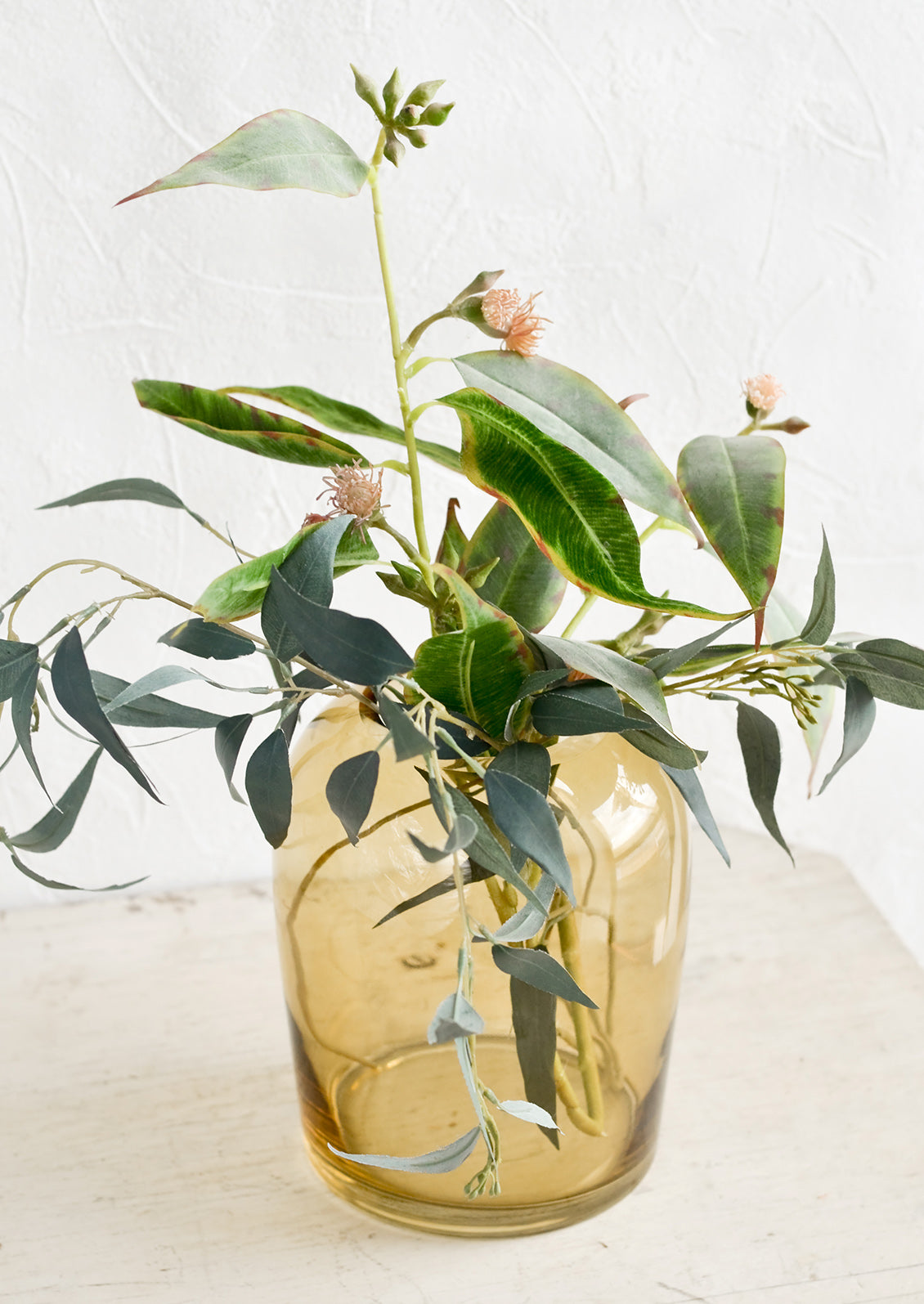 A whiskey brown glass vase with greenery.