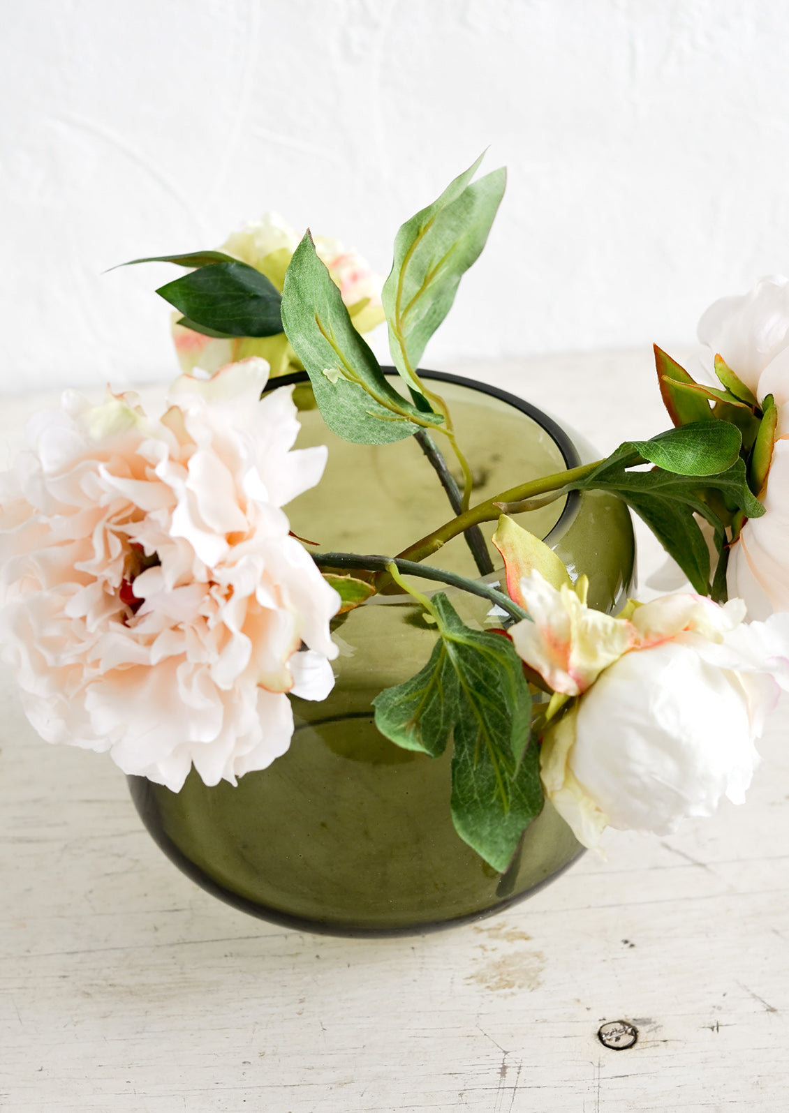 An olive green glass vase with peony flowers.