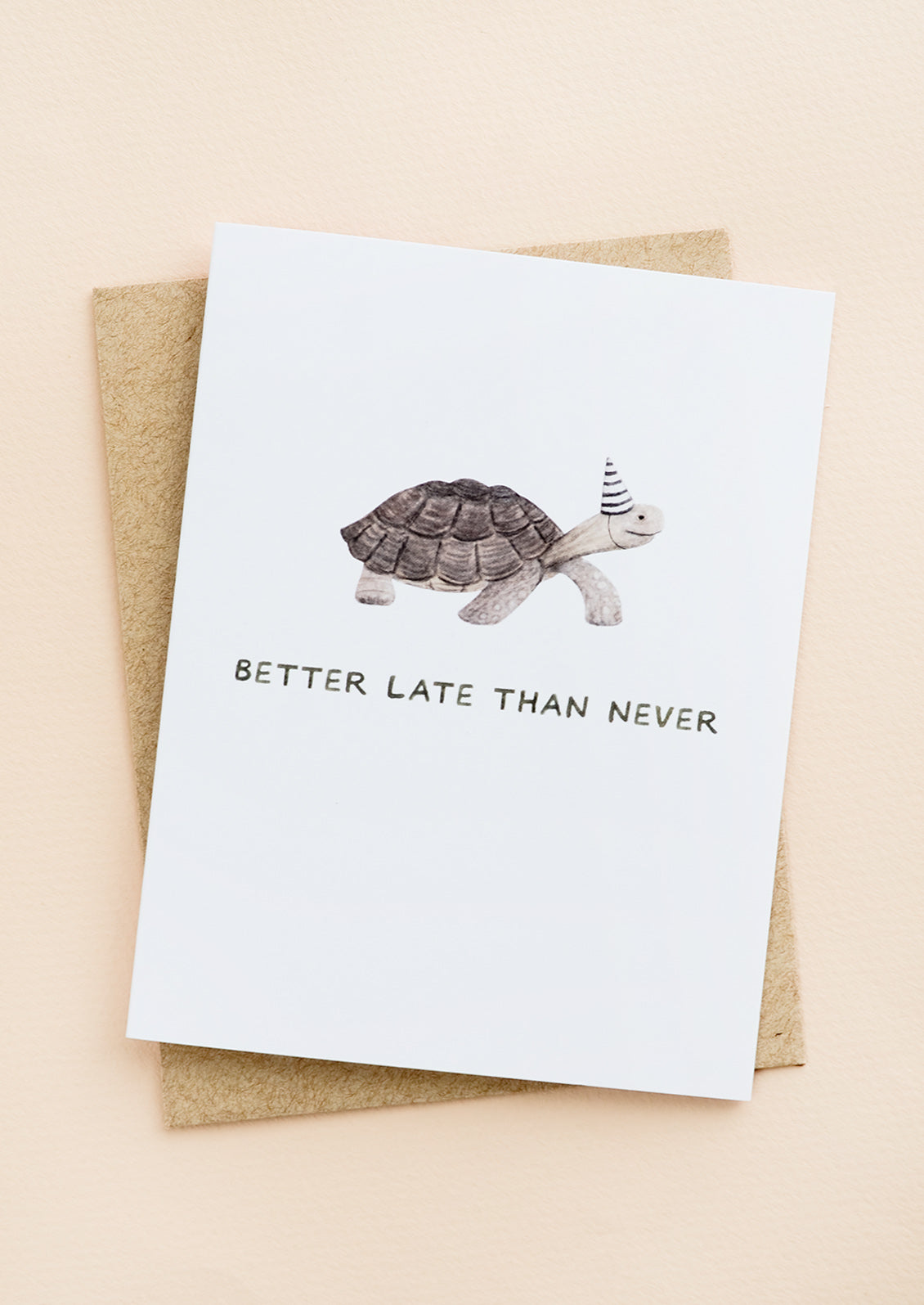 A greeting card with illustration of a tortoise in a party hat, text underneath reads "Better late than never".