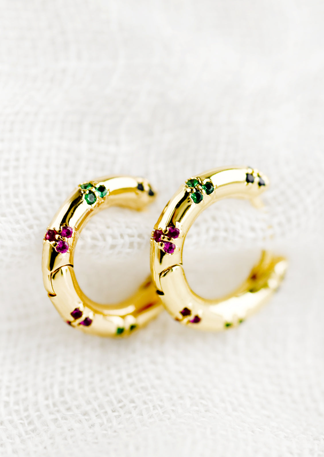 A pair of gold huggie hoops with colored crystal detailing.
