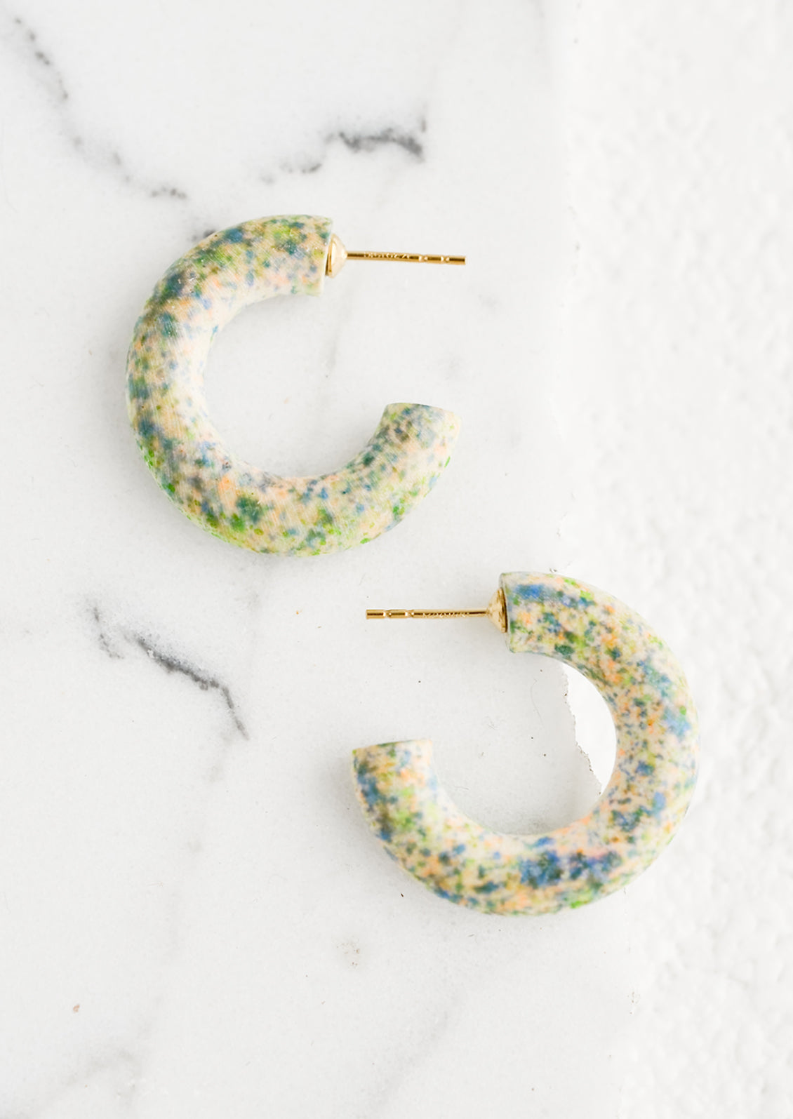 A pair of painted wood hoop earrings in speckled pattern.