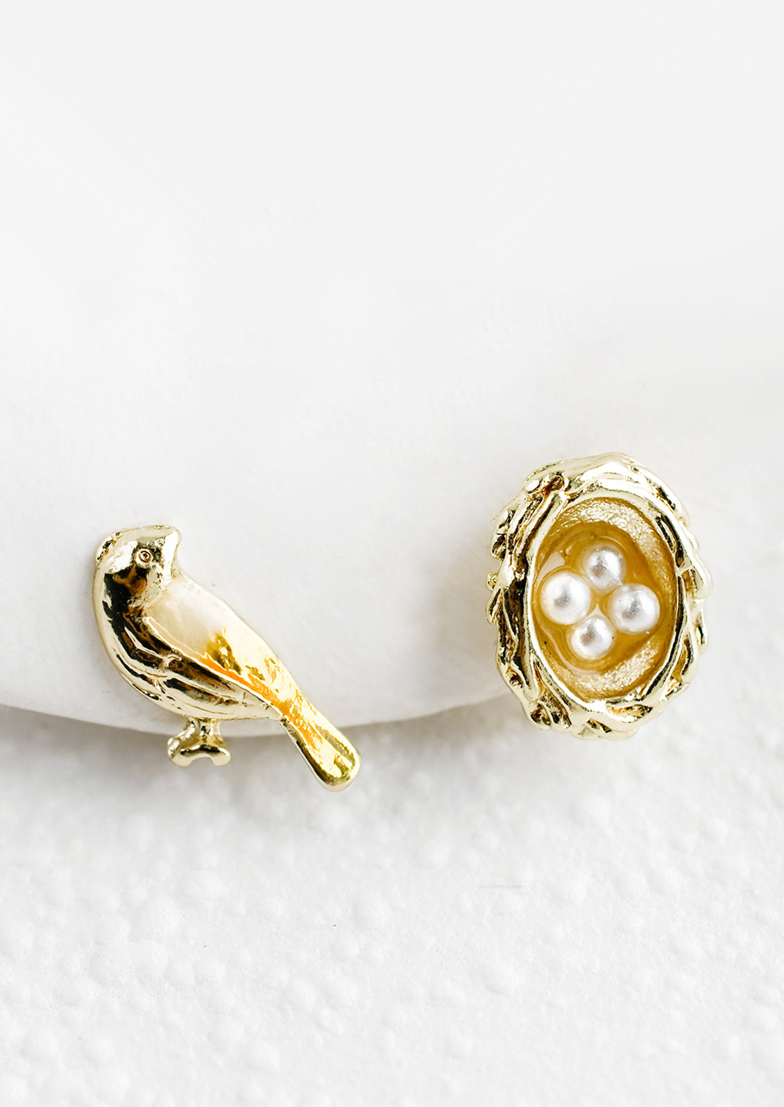A pair of stud earrings, one bird and one nest with pearl eggs.