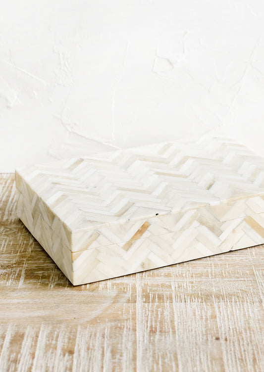 A rectangular storage box in cream colored herringbone pattern.