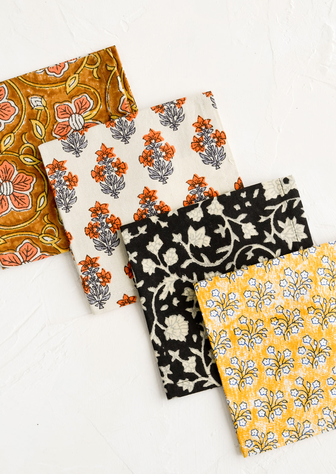 Four square fabric cocktail napkins in assorted colors and patterns.