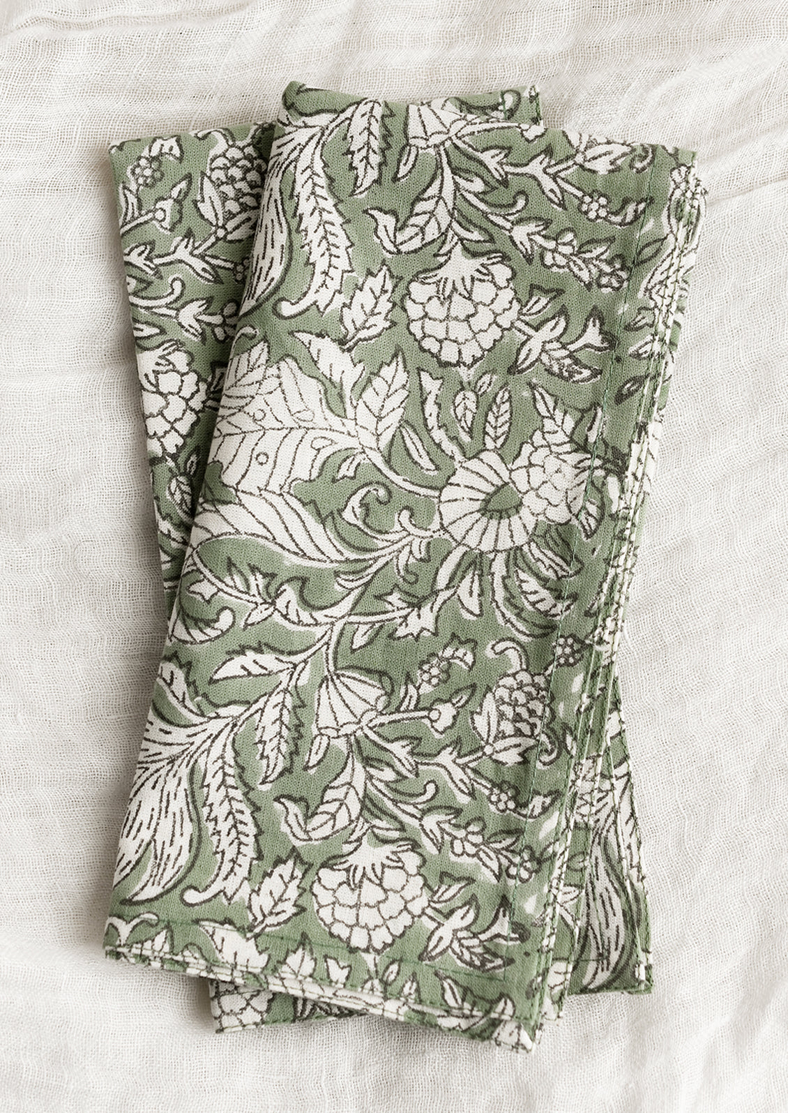 A pair of block print napkins in ivy green with black and white floral print.