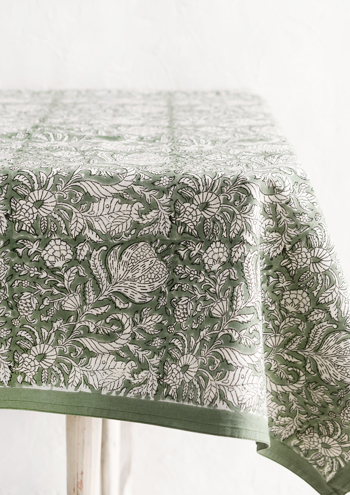 A block print tablecloth in ivy green with white and black floral print.