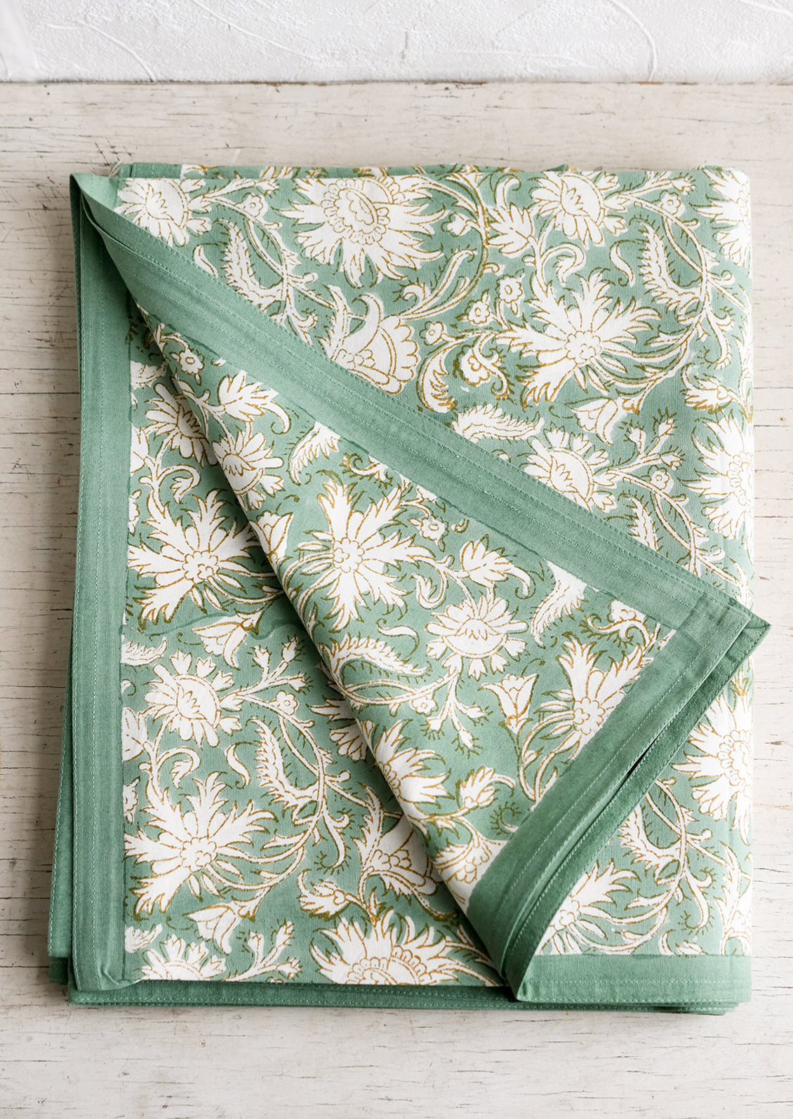 A block print tablecloth in sea green with white and brown floral print.