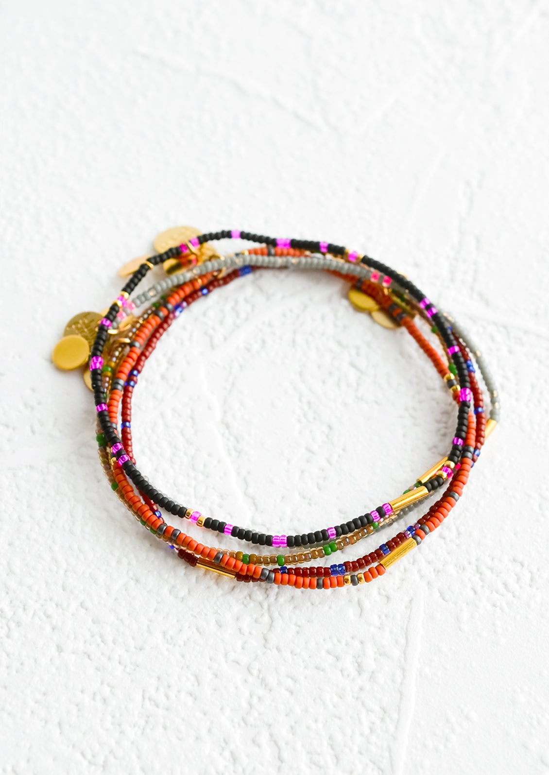 Stack of seed bead bracelets in dark colors with brass accents