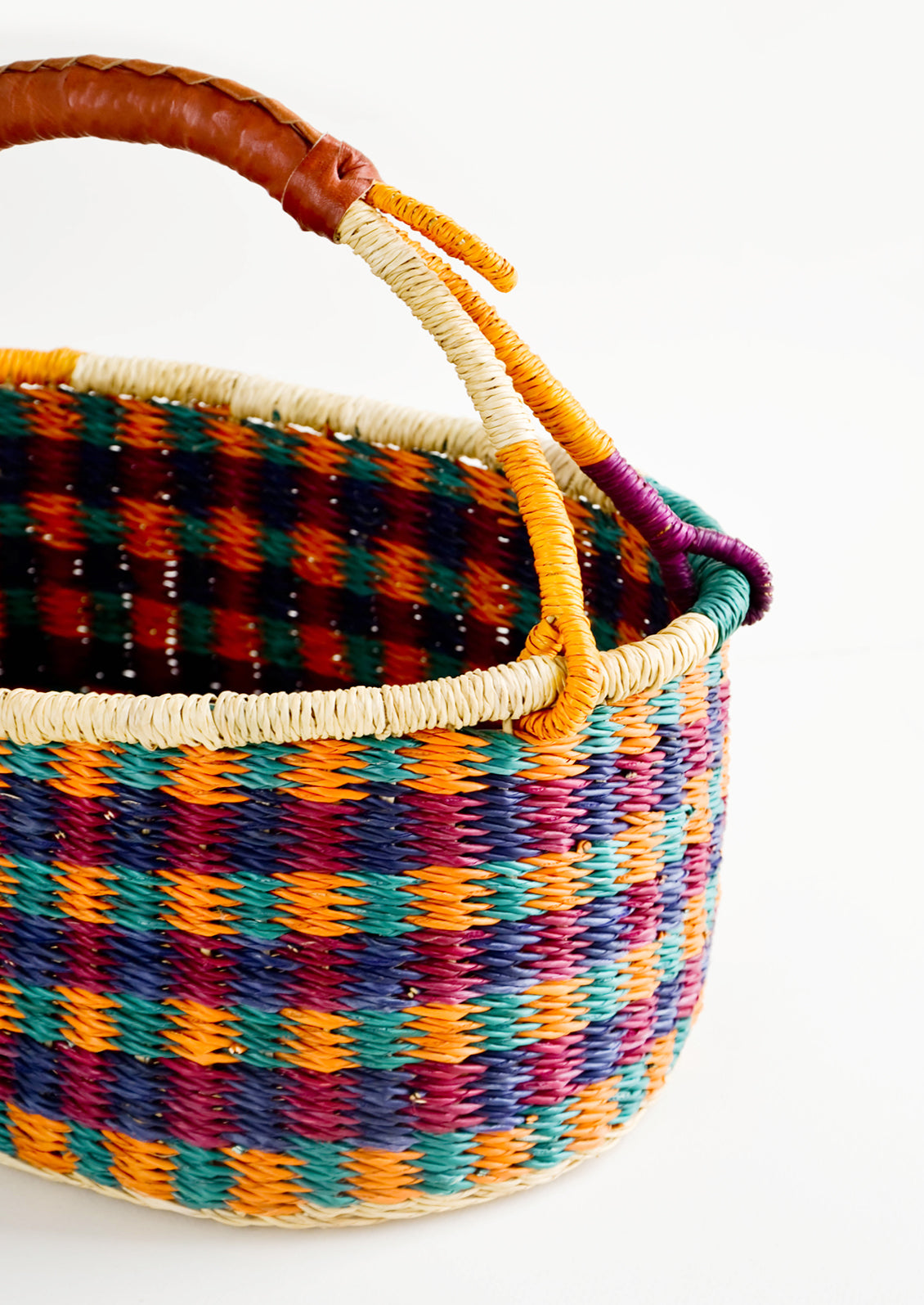 Woven basket made from multicolor dyed elephant grass with leather wrapped carrying handle