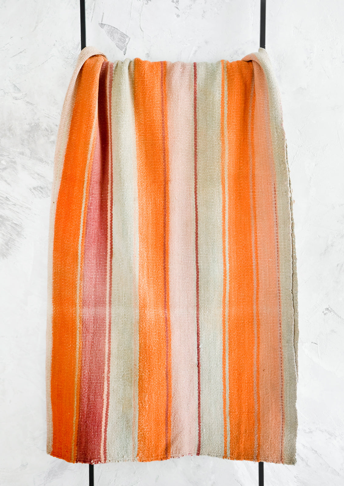 Colorful, striped woven textile intended for use as a rug or blanket, hung on a display ladder.