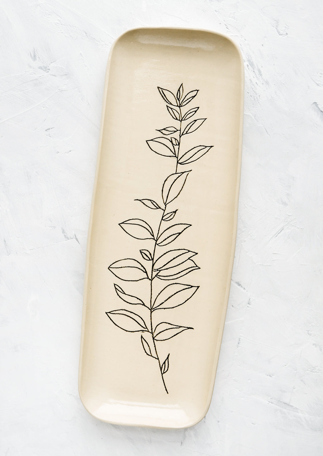 A long and skinny ceramic tray in natural bisque color with an etched black drawing of a Bay Laurel plant.