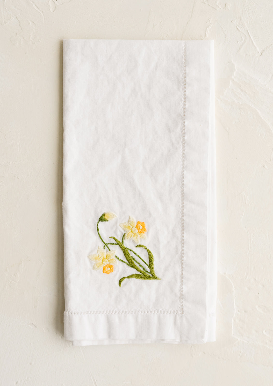 A white cotton napkin with daffodil embroidery.