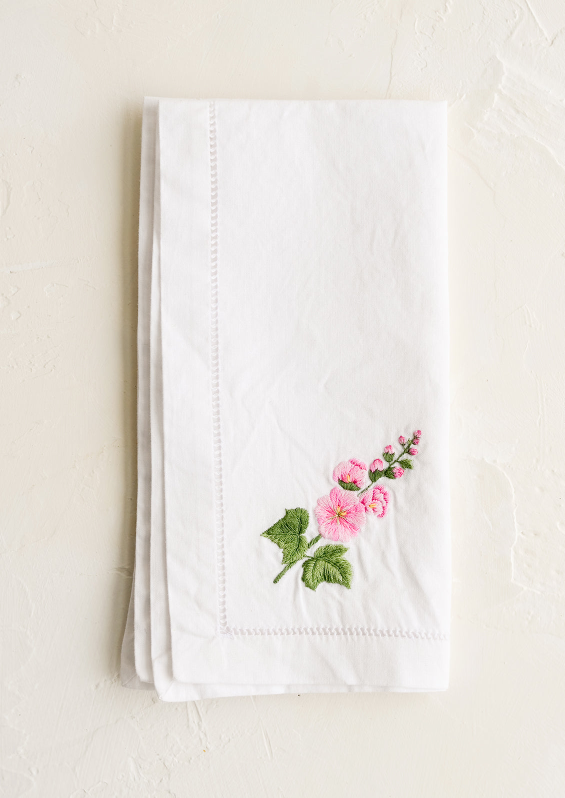 A white cotton napkin with foxglove embroidery.