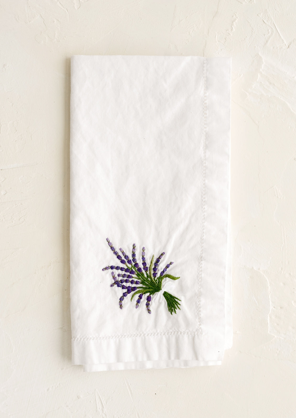 A white cotton napkin with lavender embroidery.