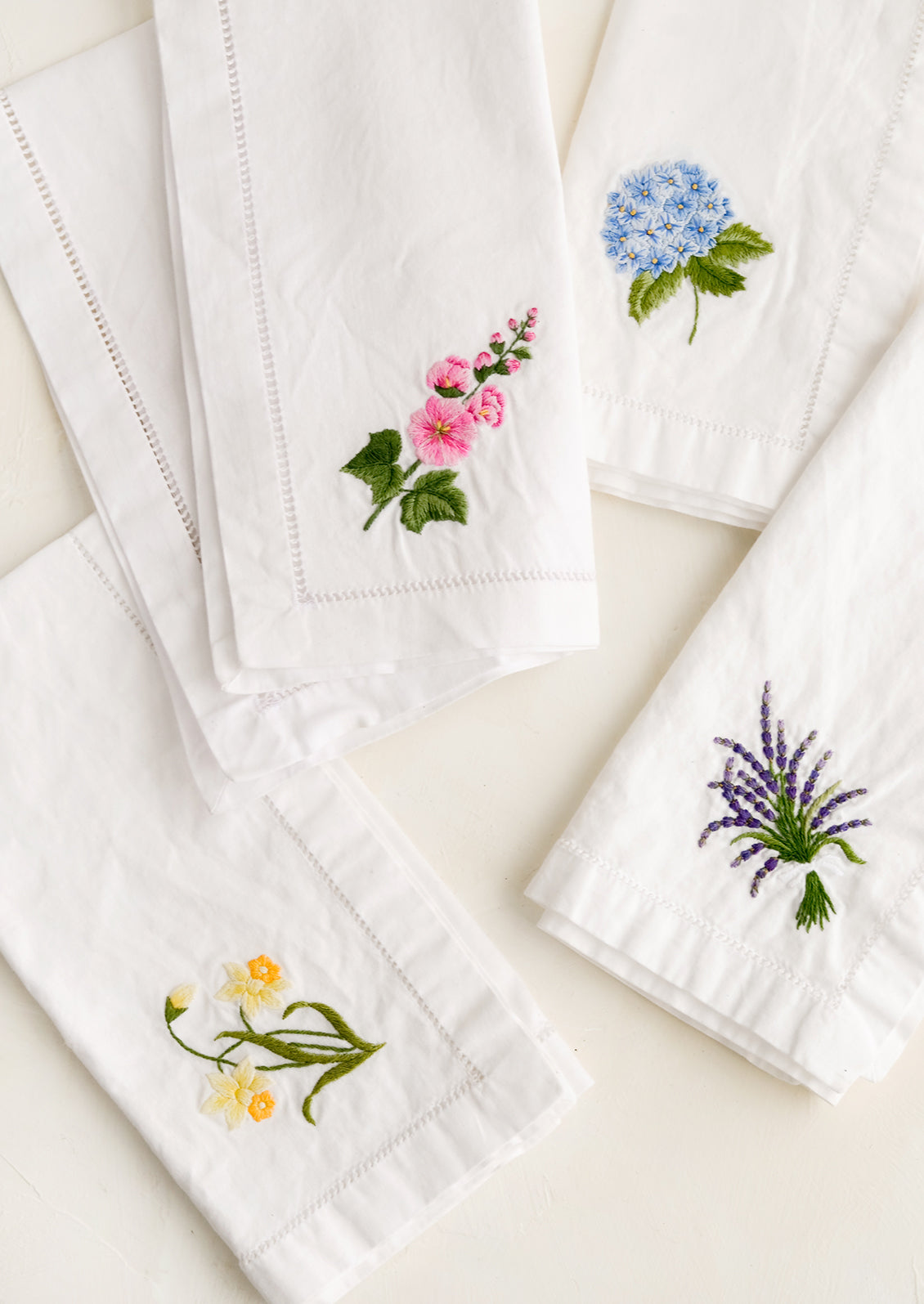 Four white cotton napkins with colorful botanical embroidery.