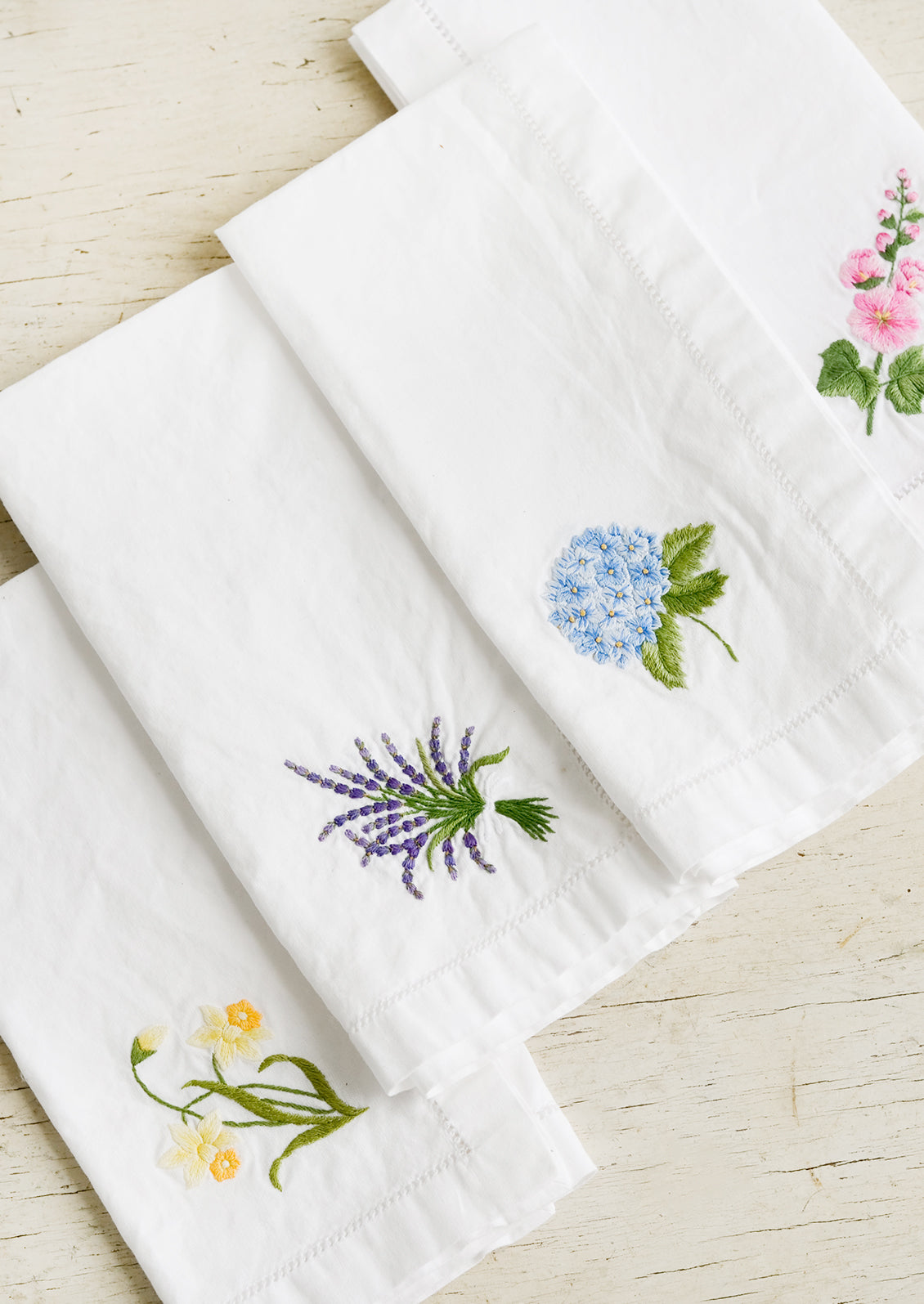 Four white cotton napkins with colorful botanical embroidery.