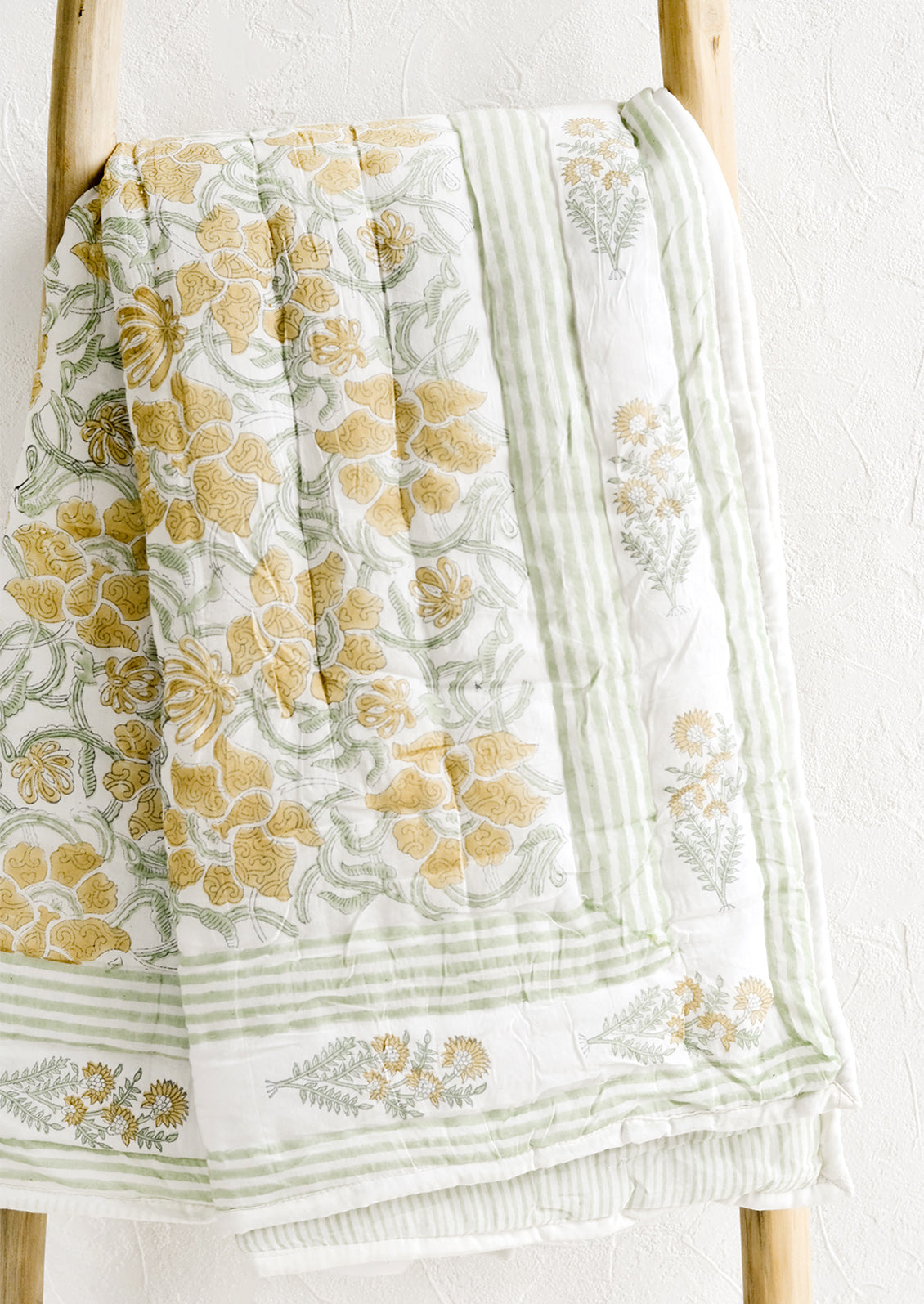 A padded quilt with block printed botanical print in green and yellow.