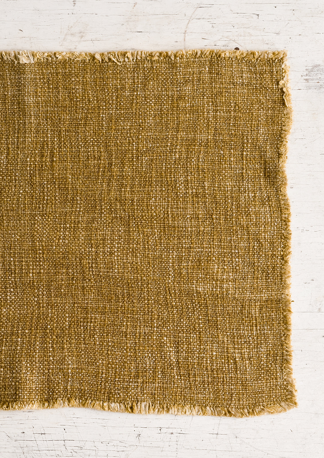 A slub boucle textured placemat in cumin yellow-brown.