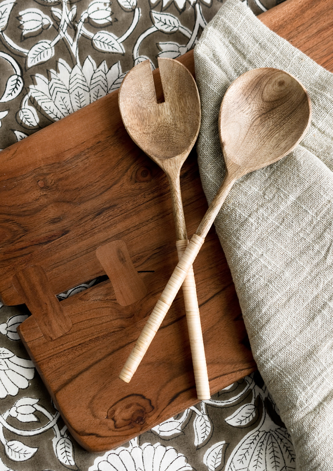 A table scene with salad servers, sage napkin and cutting board.
