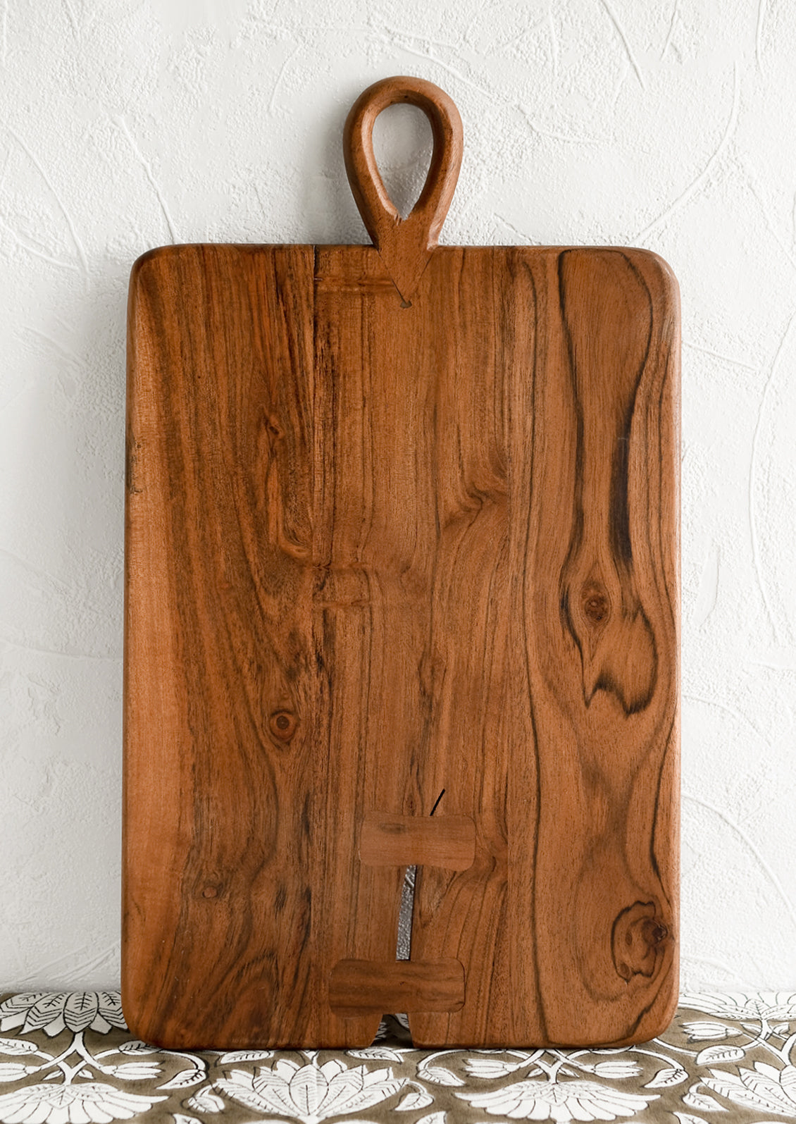 A rectangular cutting board with loop handle at top and bowtie inlay detailing.